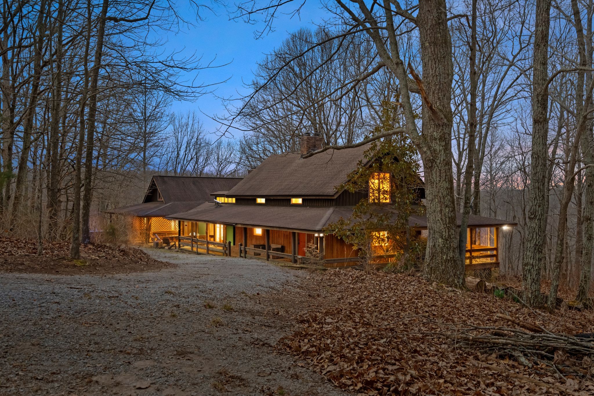 Cozy wooden cabin glowing with interior lights, tucked among bare trees at dusk.