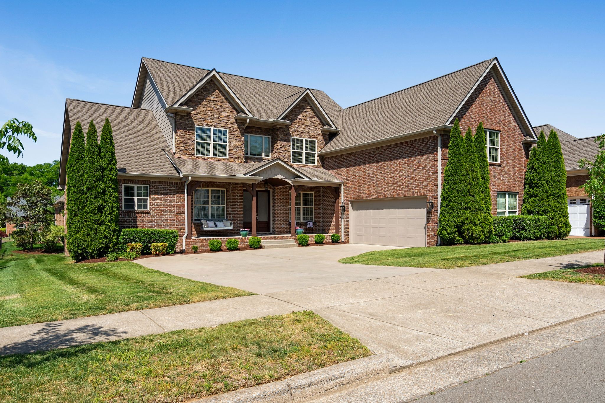 Two-story brick house with stone façade, gabled roof, front porch, and a two-car garage, well-kept lawn.